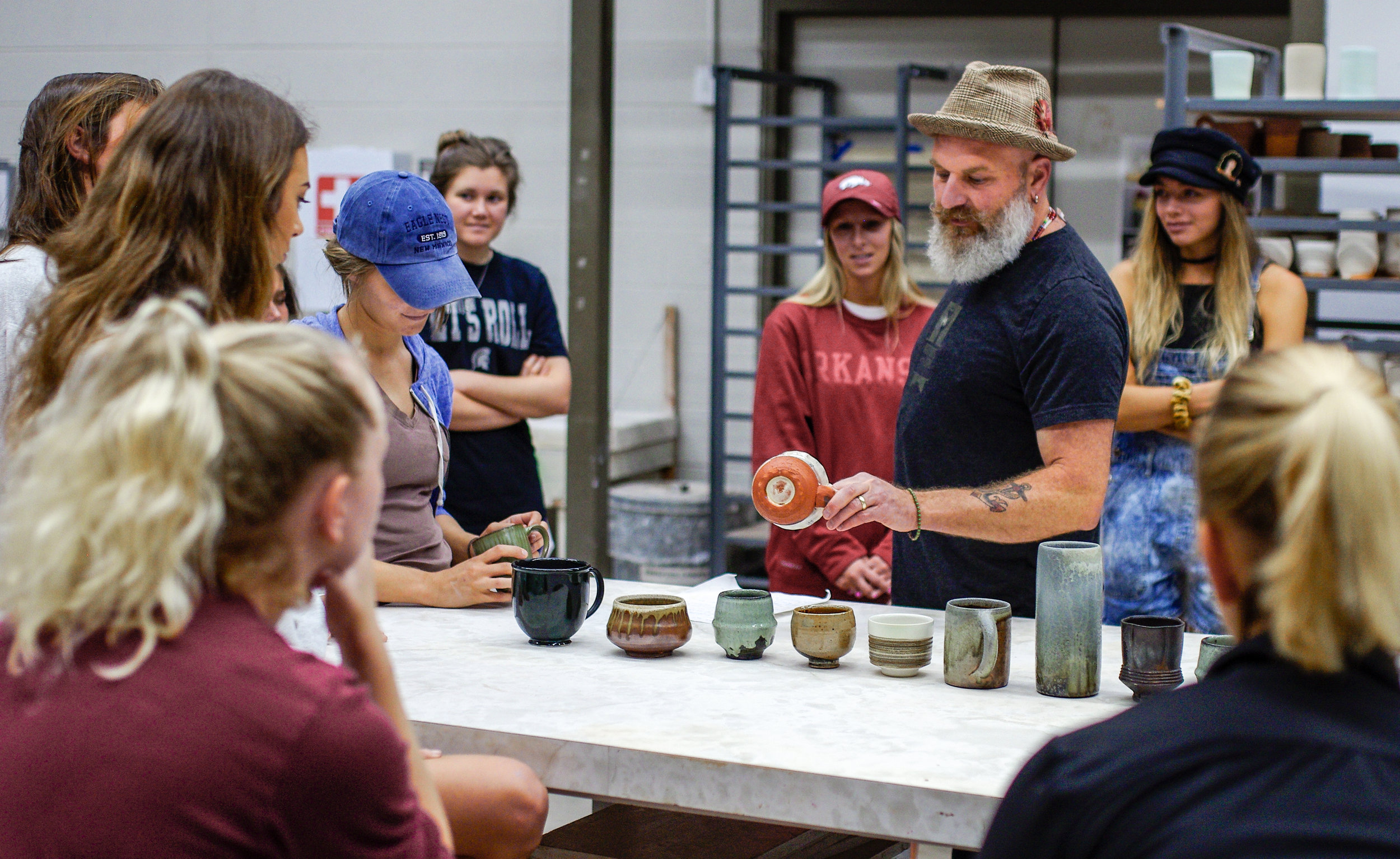 Ceramics faculty Adam Posnak holding ceramic mug and teaching a group of students