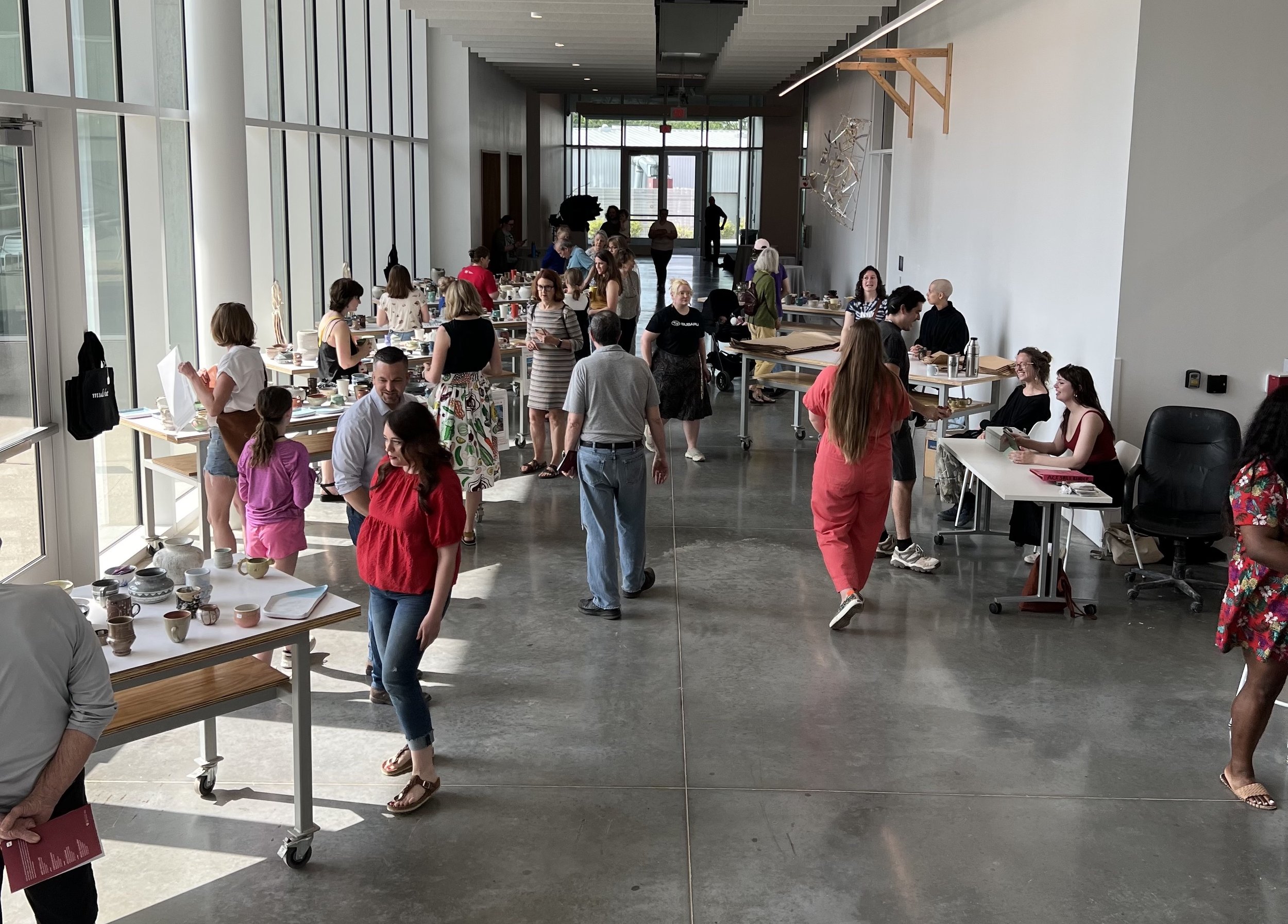 People walking through long corridor looking at tables filled with ceramic pieces